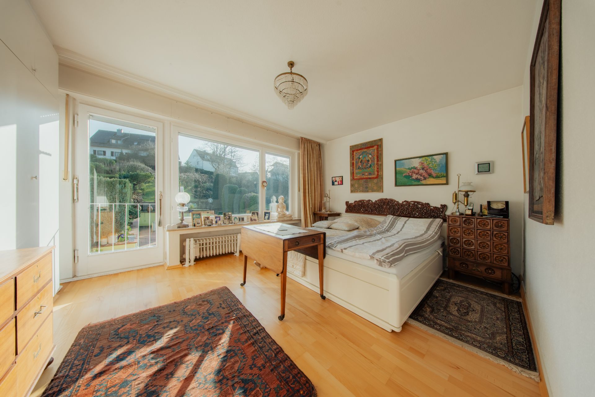 Helles Schlafzimmer mit großem Fenster, Doppelbett, Holzmöbeln und dekorativen Bildern an der Wand.