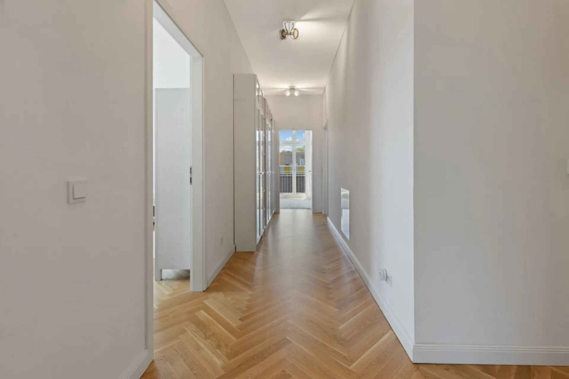 Heller Flur mit Parkettboden und Glastüren am Ende, seitlich zwei Türen.