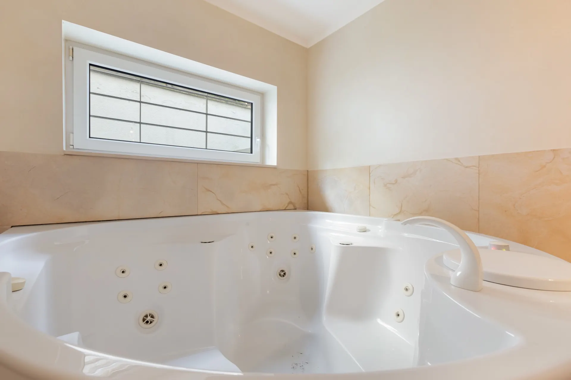 Moderne Whirlpool-Badewanne in einem hellen Badezimmer mit kleinem Fenster.