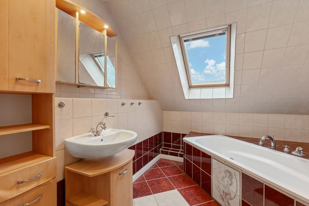 Badezimmer mit Dachfenster, Waschbecken, Spiegel, Holzmöbeln und Badewanne mit roten Fliesen.