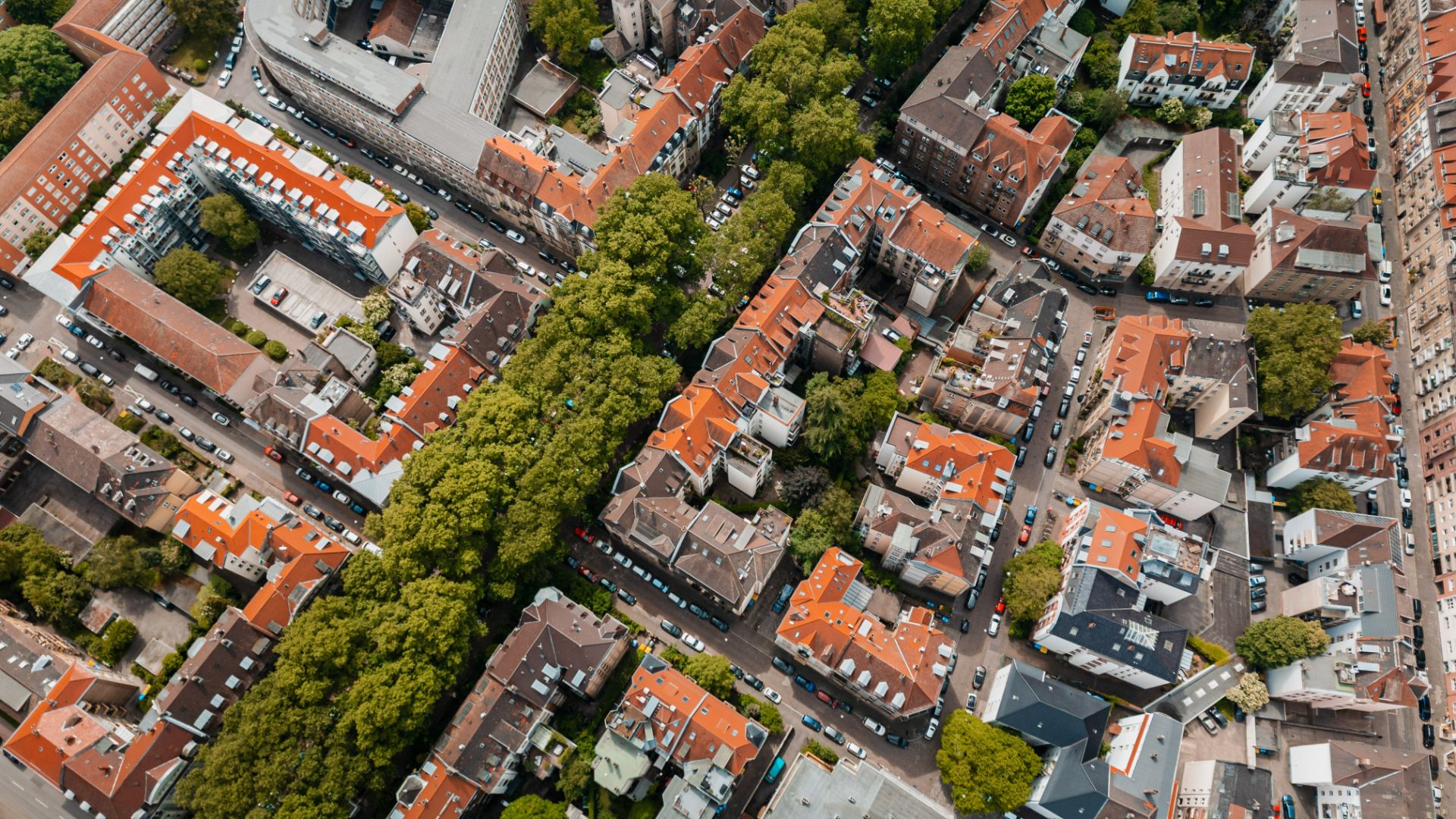 Luftaufnahme eines Wohngebiets mit roten Dächern und vielen Bäumen entlang der Straßen.