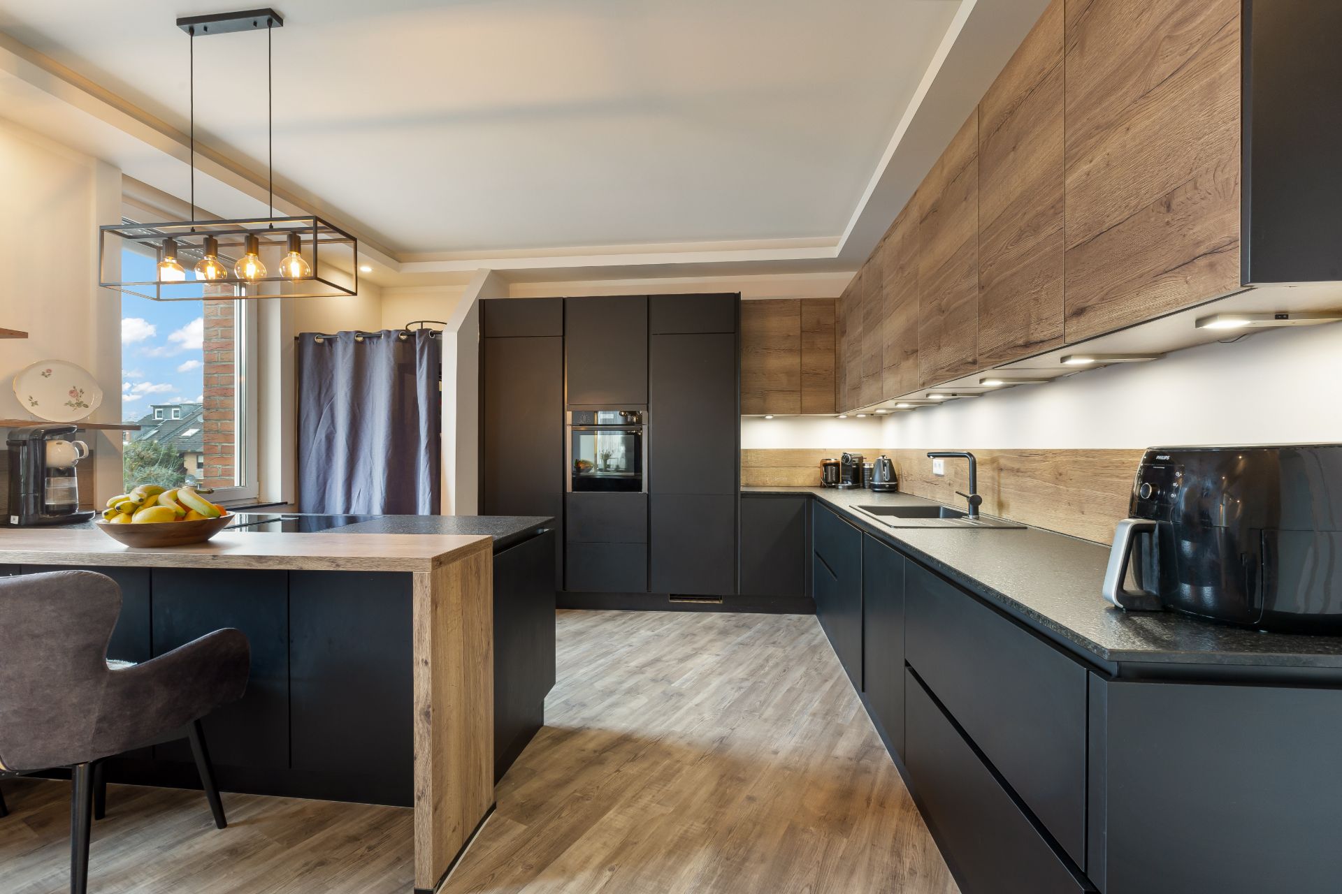 Moderne Küche mit Holzboden, dunklen Schränken und einer Kücheninsel mit Sitzplatz.