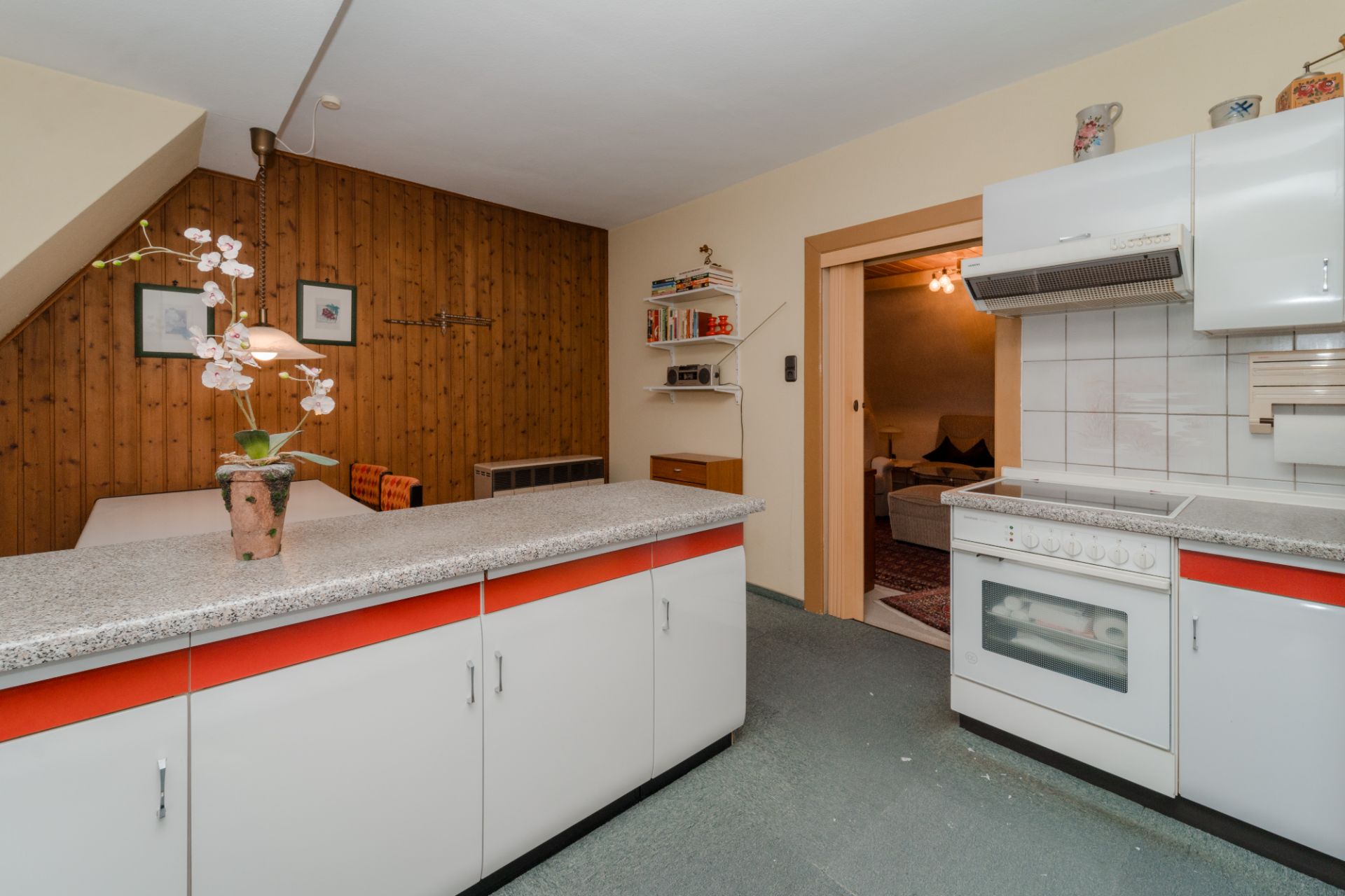 Küche mit weiß-roten Schränken, Essbereich mit Holzverkleidung und Dekoblumen auf der Theke.