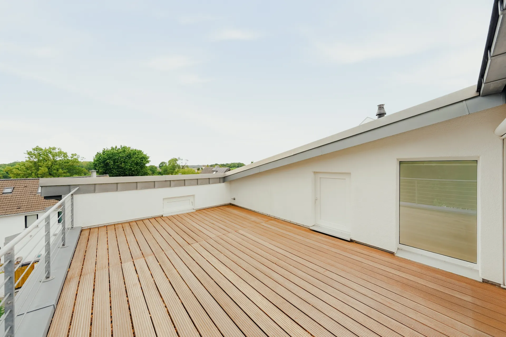 Große Dachterrasse mit Holzbelag und Geländer, angrenzend an ein weißes Haus.
