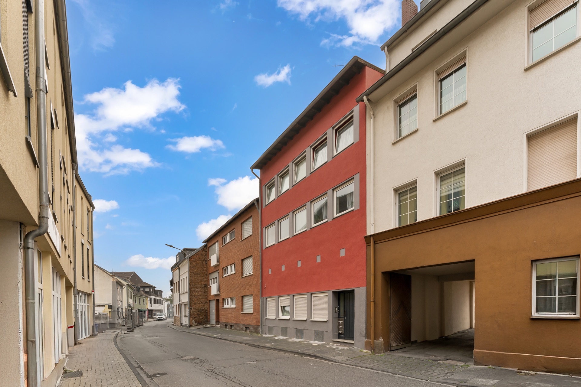 Straße mit mehrstöckigen Wohnhäusern, eines davon rot gestrichen, bei Tageslicht.