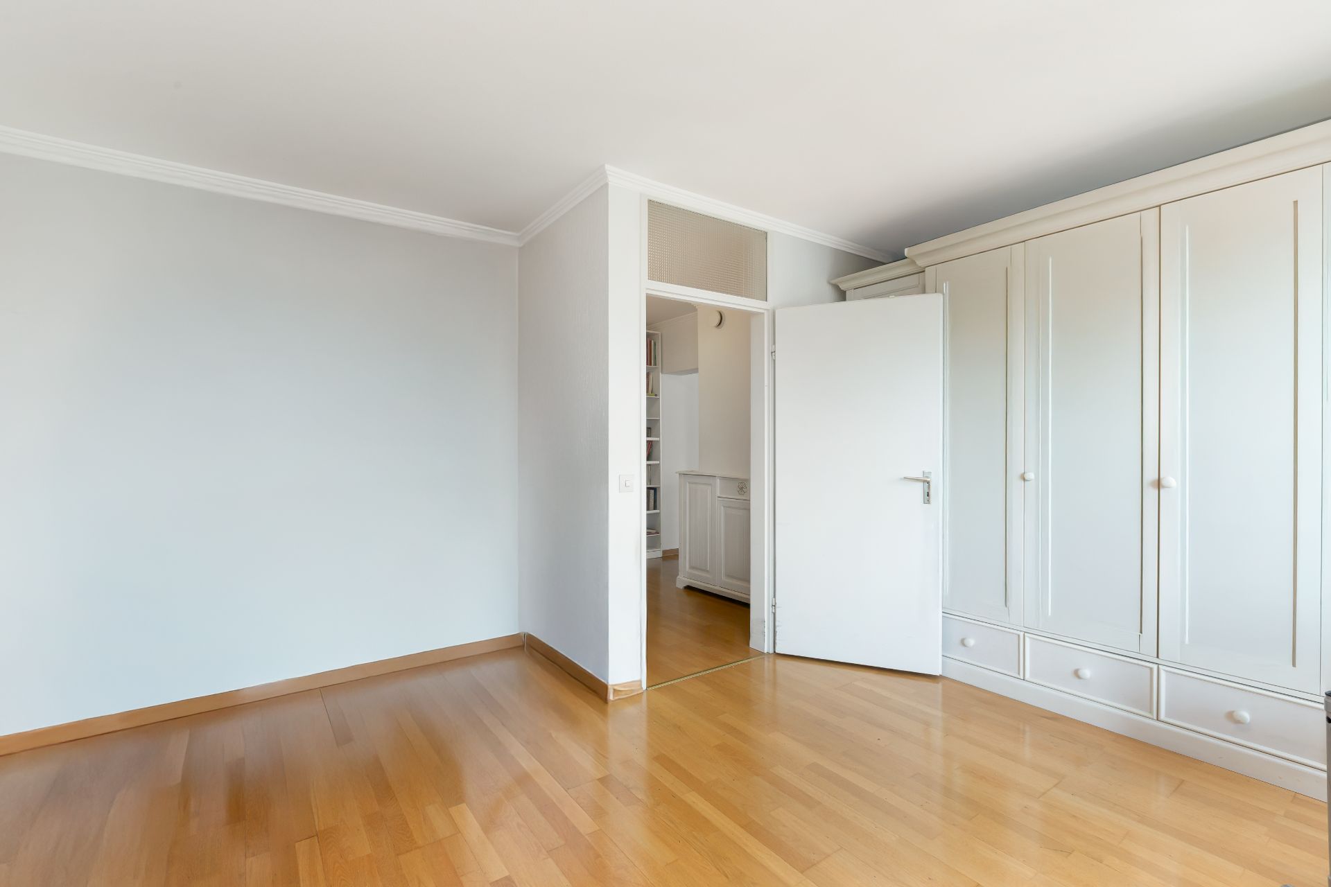 Leeres Zimmer mit Holzfußboden, weißer Wand und großem weißen Kleiderschrank.
