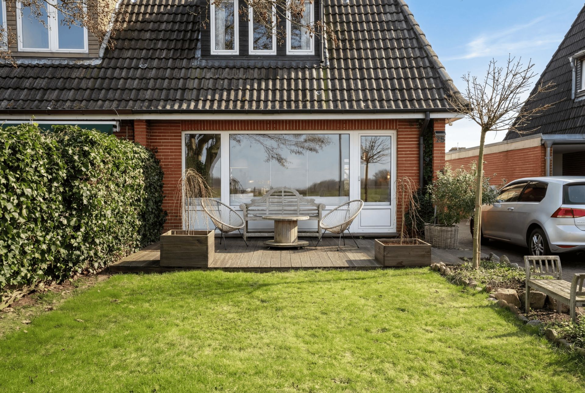 Garten mit Terrasse, rundem Tisch und Stühlen vor einem Backsteinhaus mit großen Fenstern.