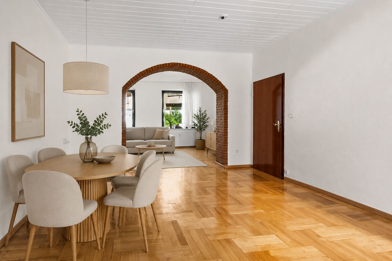 Essbereich mit rundem Tisch und Stühlen, offener Durchgang zum Wohnzimmer mit Sofa und Fenster.