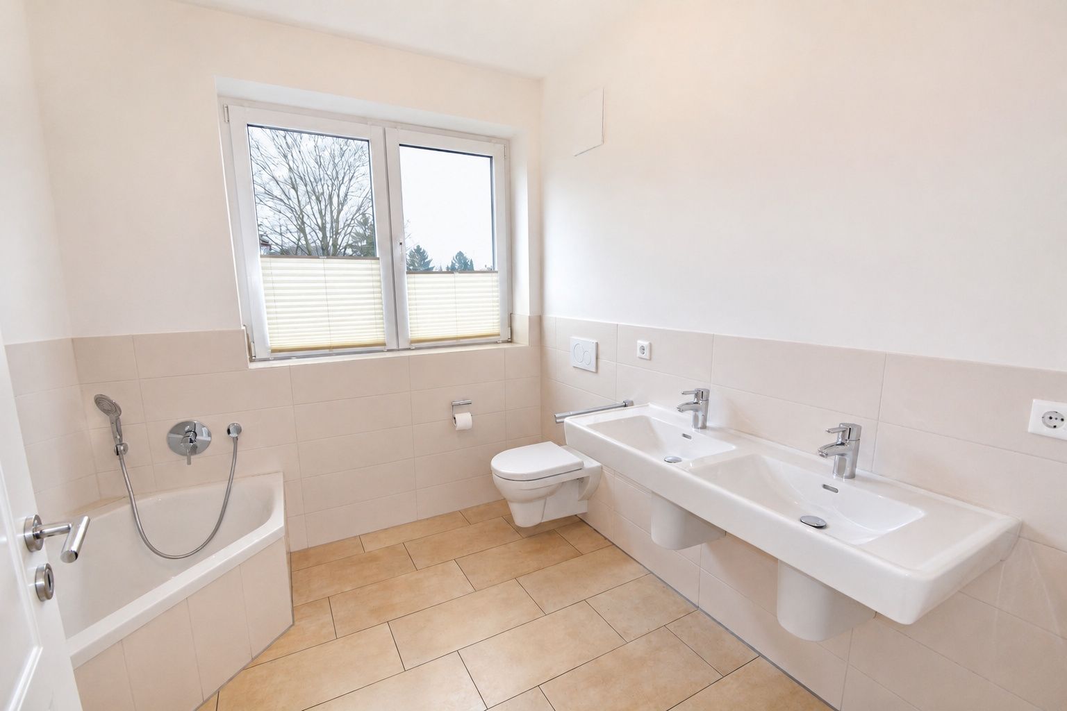 Helles Bad mit Badewanne, Doppellavabo, Toilette und Fenster.