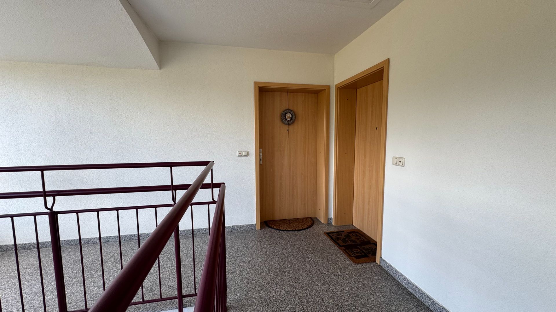 Hausflur mit zwei Holztüren, Türmatten und einem Treppengeländer.
