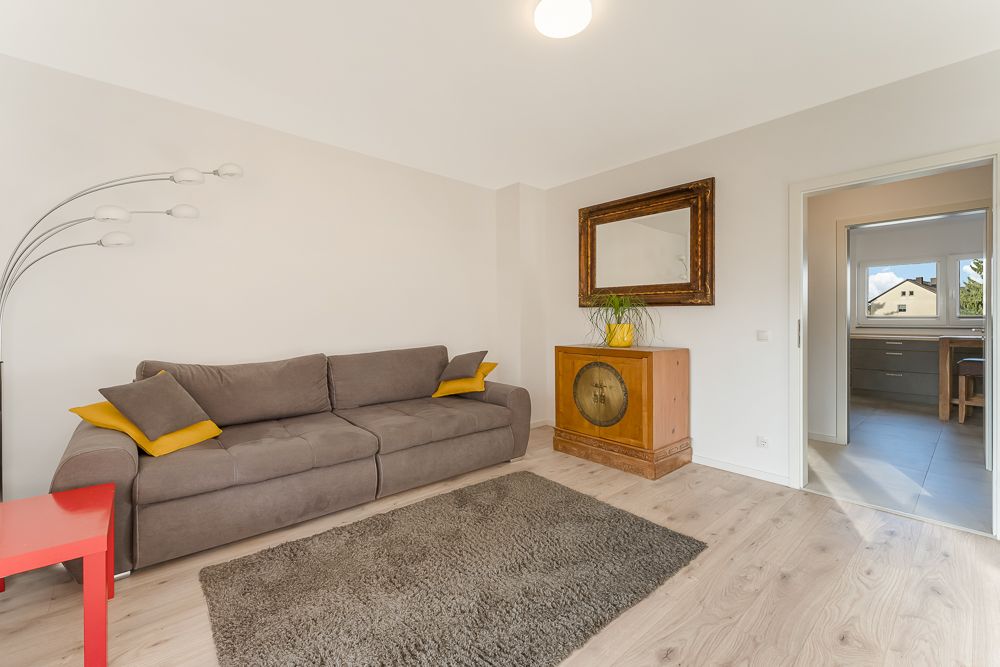Wohnzimmer mit grauem Sofa, gelben Kissen, Teppich, Stehlampe und Kommode mit Spiegel.