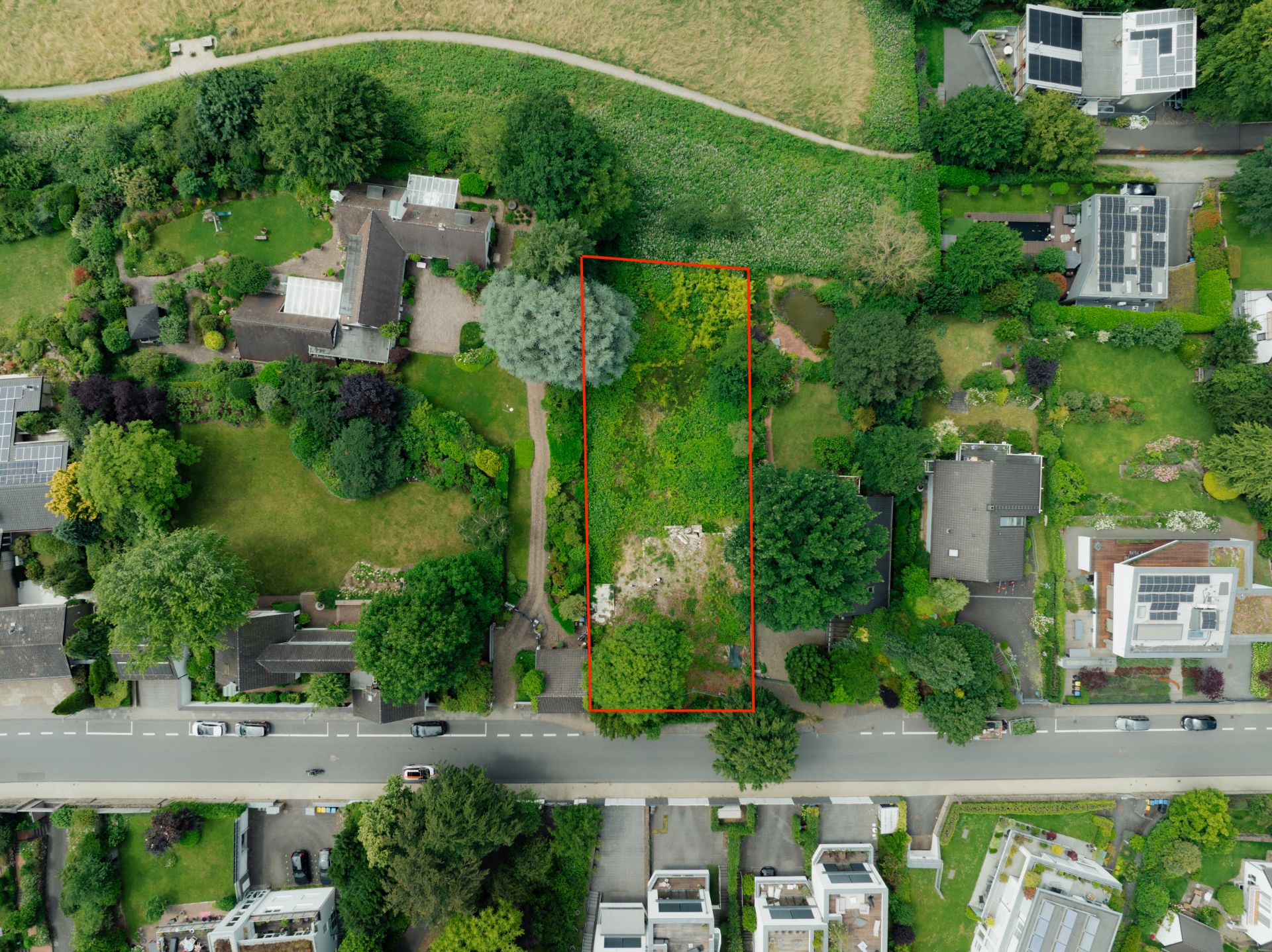 Luftaufnahme eines rechteckigen Gartengrundstücks mit Bäumen und Rasen, rot umrandet.
