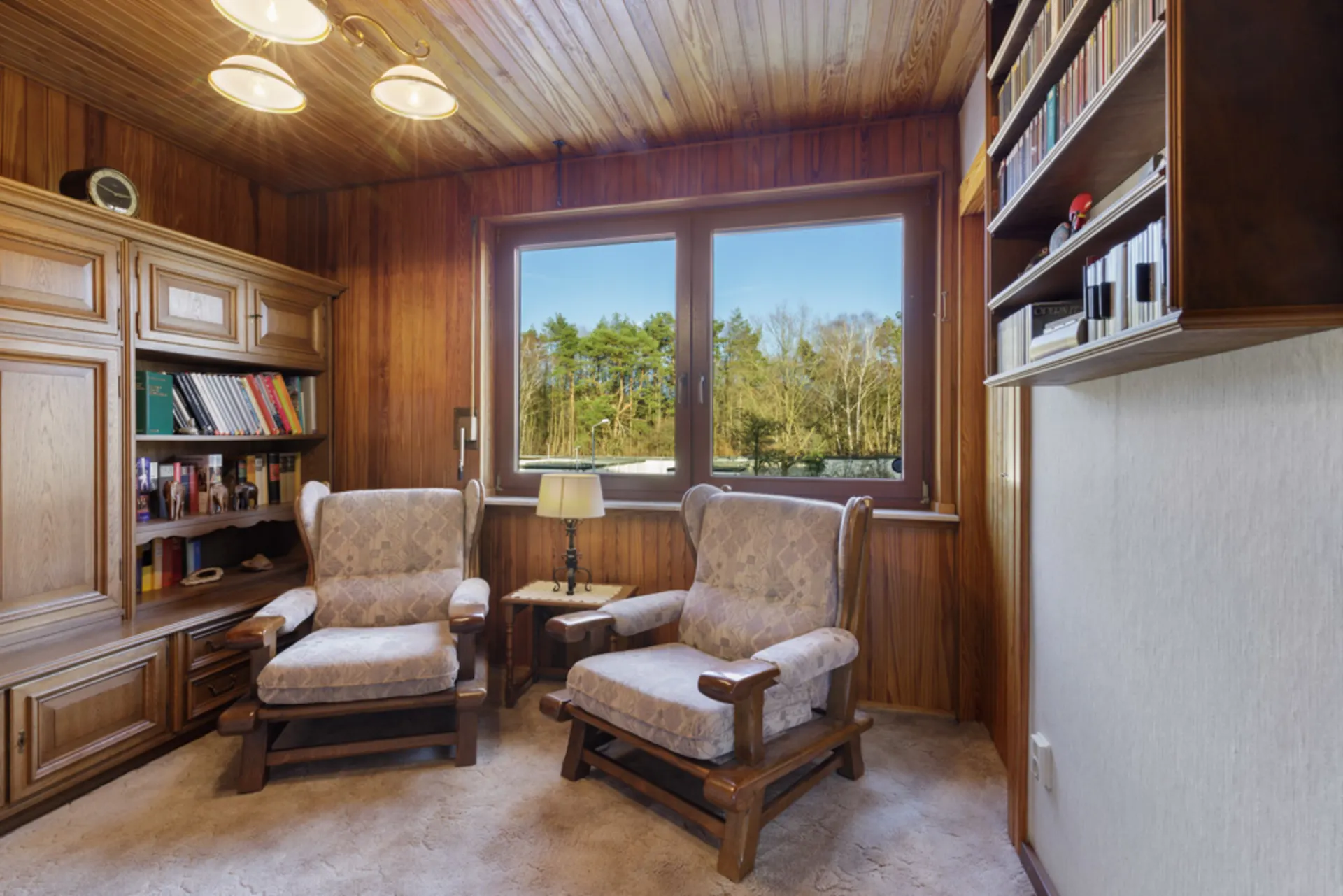 Gemütliches Zimmer mit zwei Sesseln, Holzregalen, Fenstern und Ausblick auf Bäume.