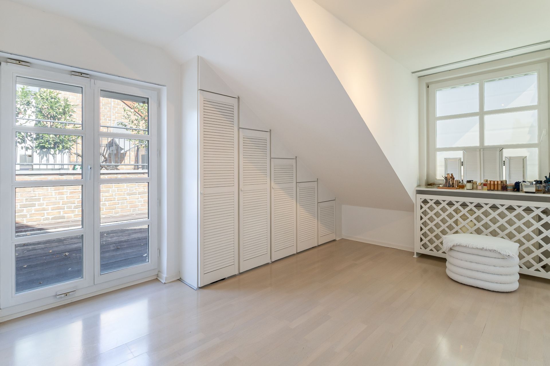 Helles Zimmer mit Fenster, Stauschrank unter Schräge und Kommode, auf der ein Spiegel steht.