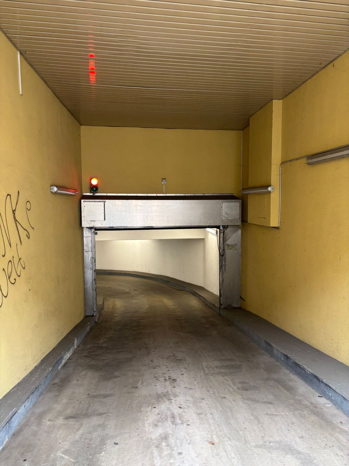 Einfahrt zu einer Tiefgarage mit gelben Wänden und einer roten Ampel.