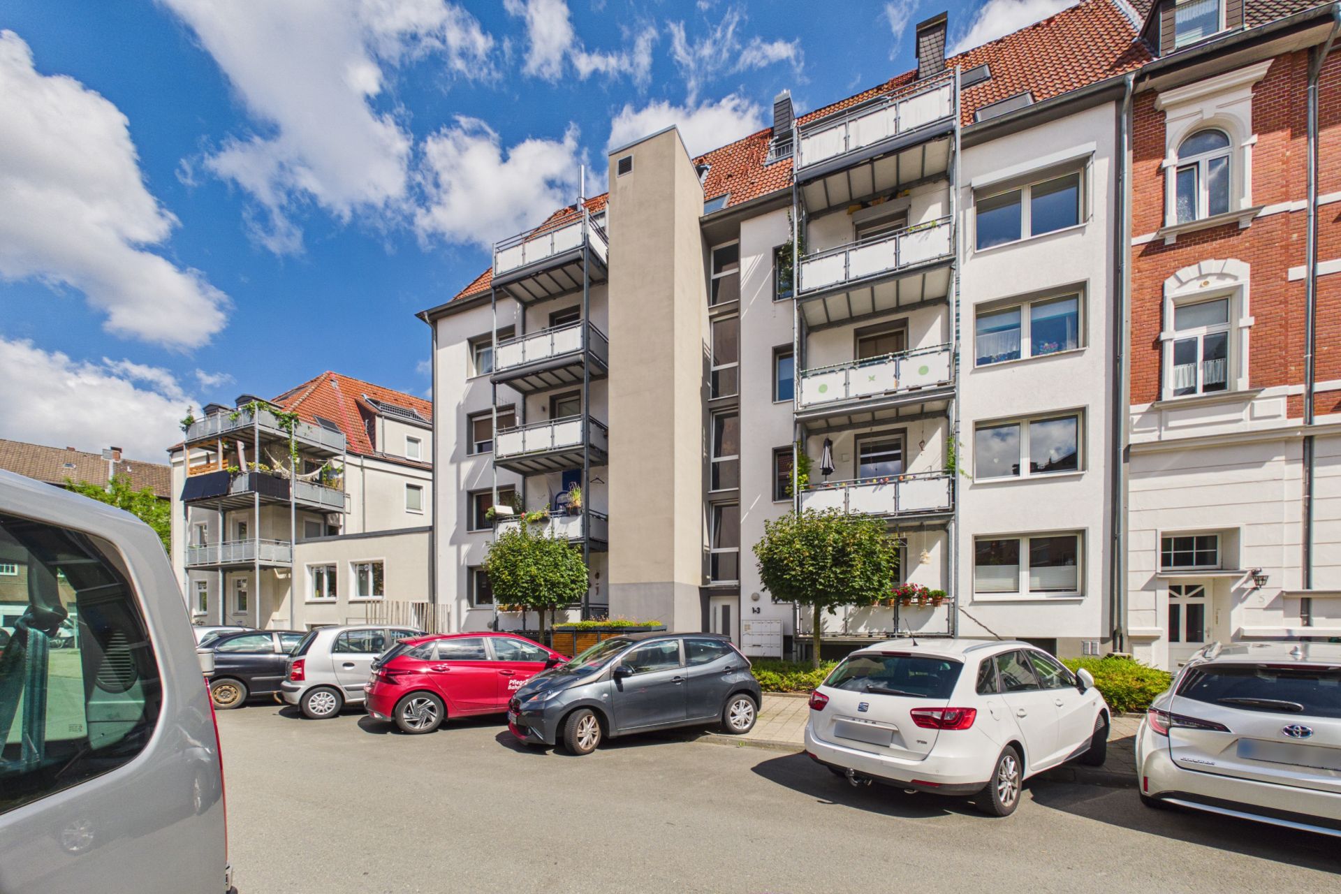 Mehrstöckiges Wohngebäude mit Balkonen und parkenden Autos davor.