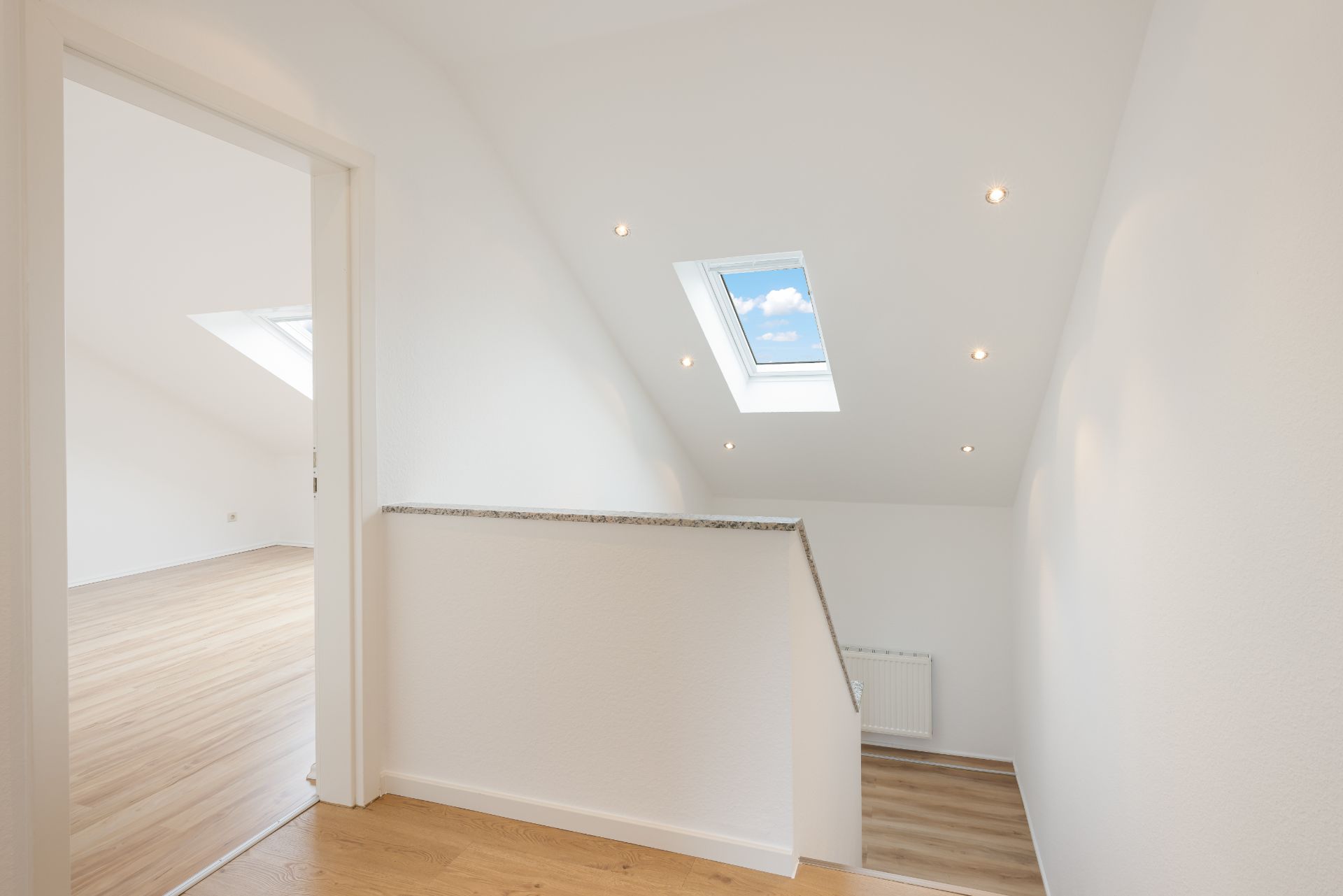 Helle Dachgeschossflur mit Dachfenster und Holzfußboden, Tür zu weiterem Raum.