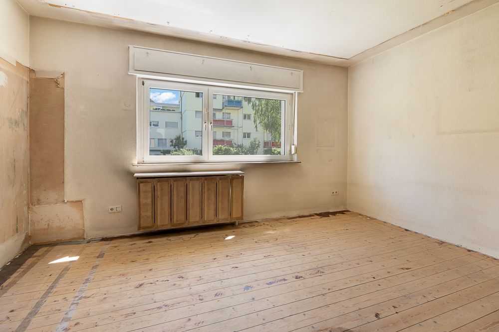 Leerer Raum mit Holzboden, großem Fenster und Heizkörper darunter.