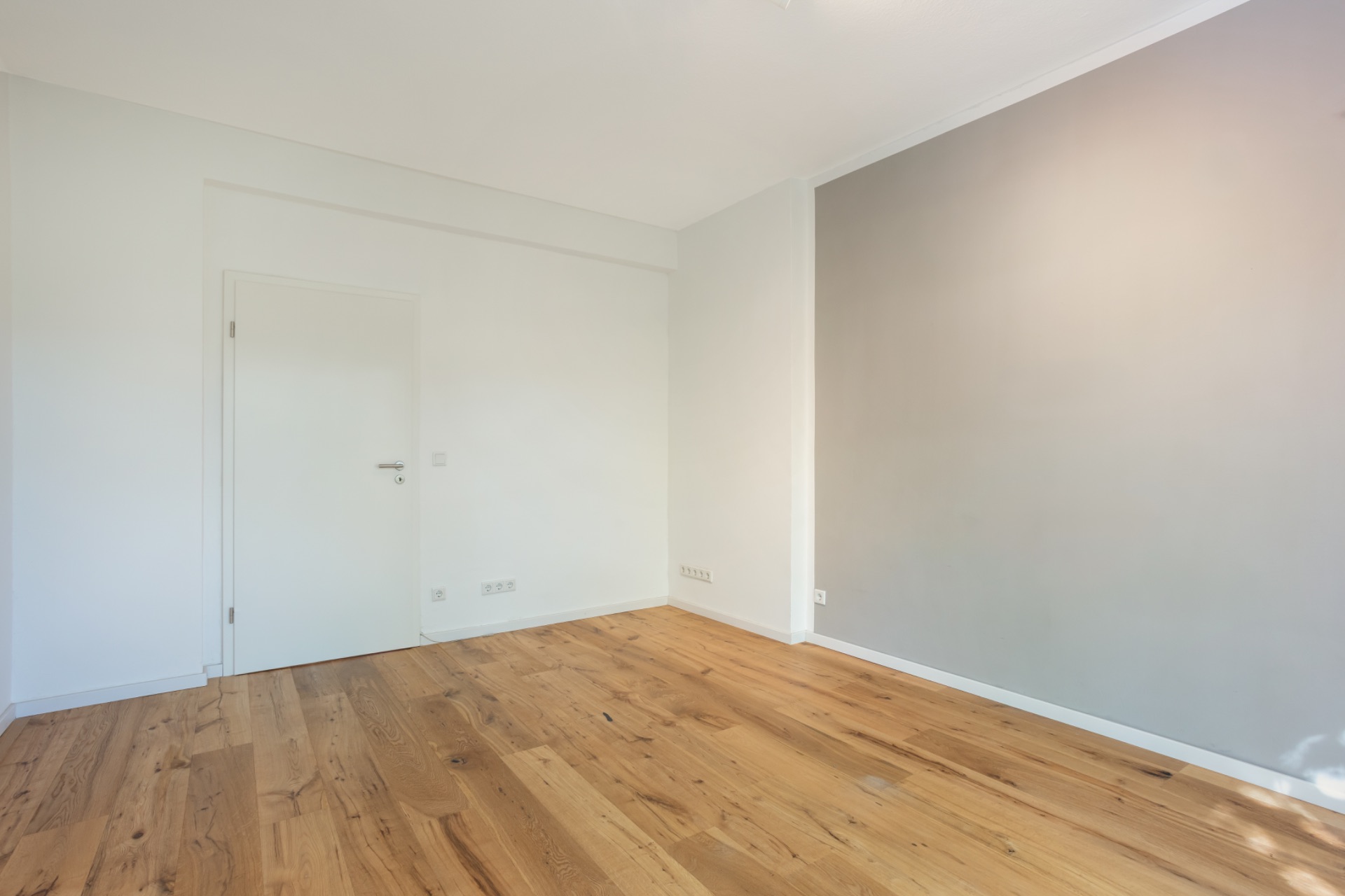 Leerer Raum mit Holzboden, weißen Wänden und einer grauen Akzentwand.