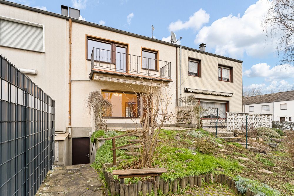 Rückansicht eines Reihenhauses mit Balkon, Terrasse und kleinem Garten mit Weg.