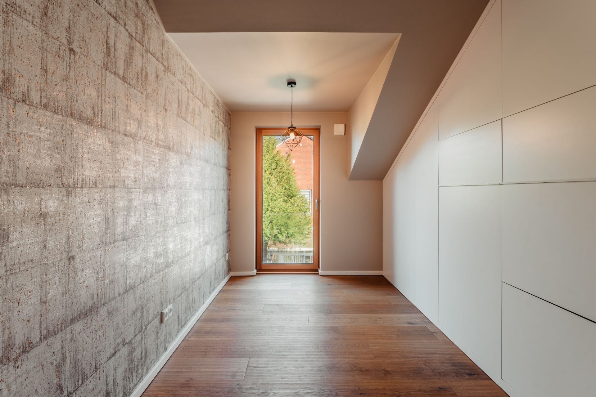 Leerer Raum mit Holzfußboden, großer Fensterfront und grauer Strukturwand.