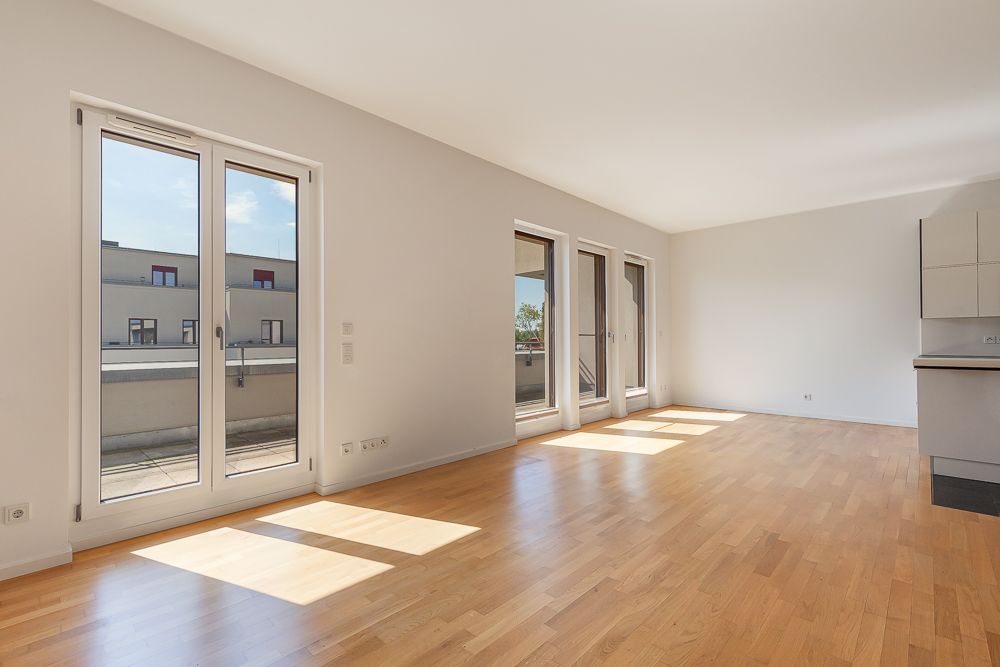 Heller Raum mit Holzboden, großen Fenstern und Zugang zu einem Balkon.