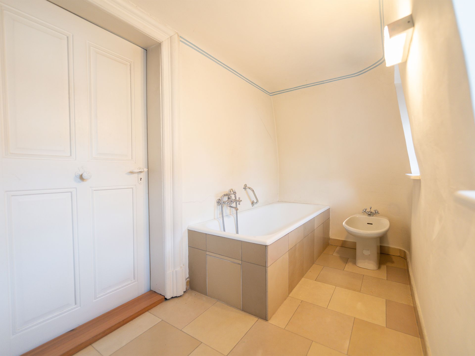 Helles Badezimmer mit Badewanne, Bidet und weißer Tür.