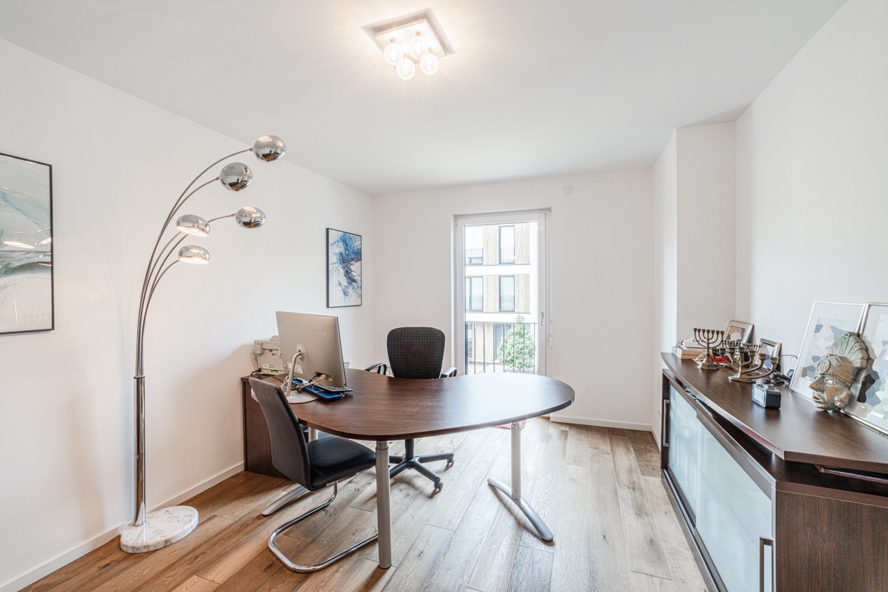 Modernes Arbeitszimmer mit großem Schreibtisch, Computer und Stehlampe auf Holzfußboden.