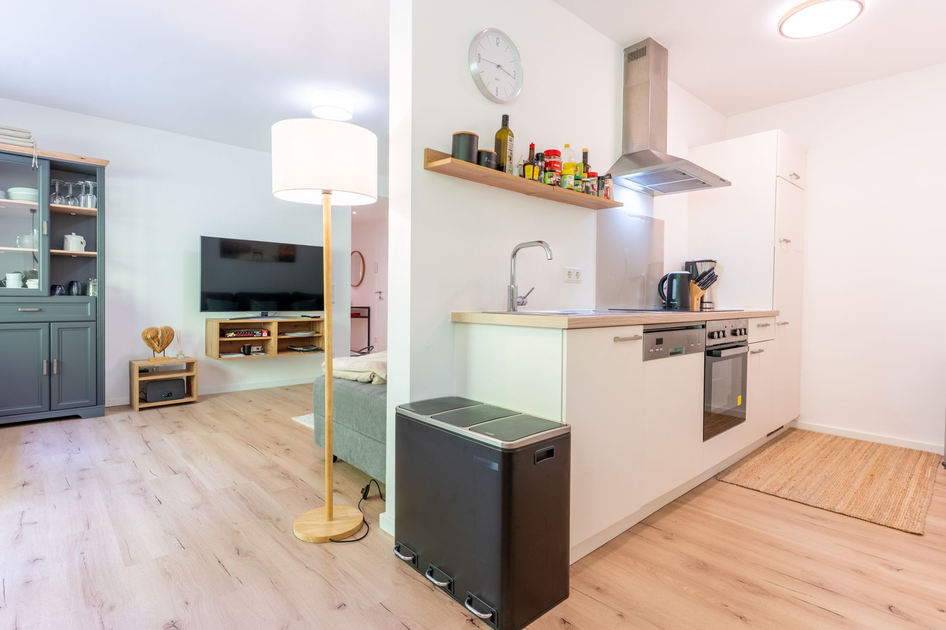 Helle Wohnküche mit Einbauküche, Stehlampe, Fernseher und Holzfußboden.
