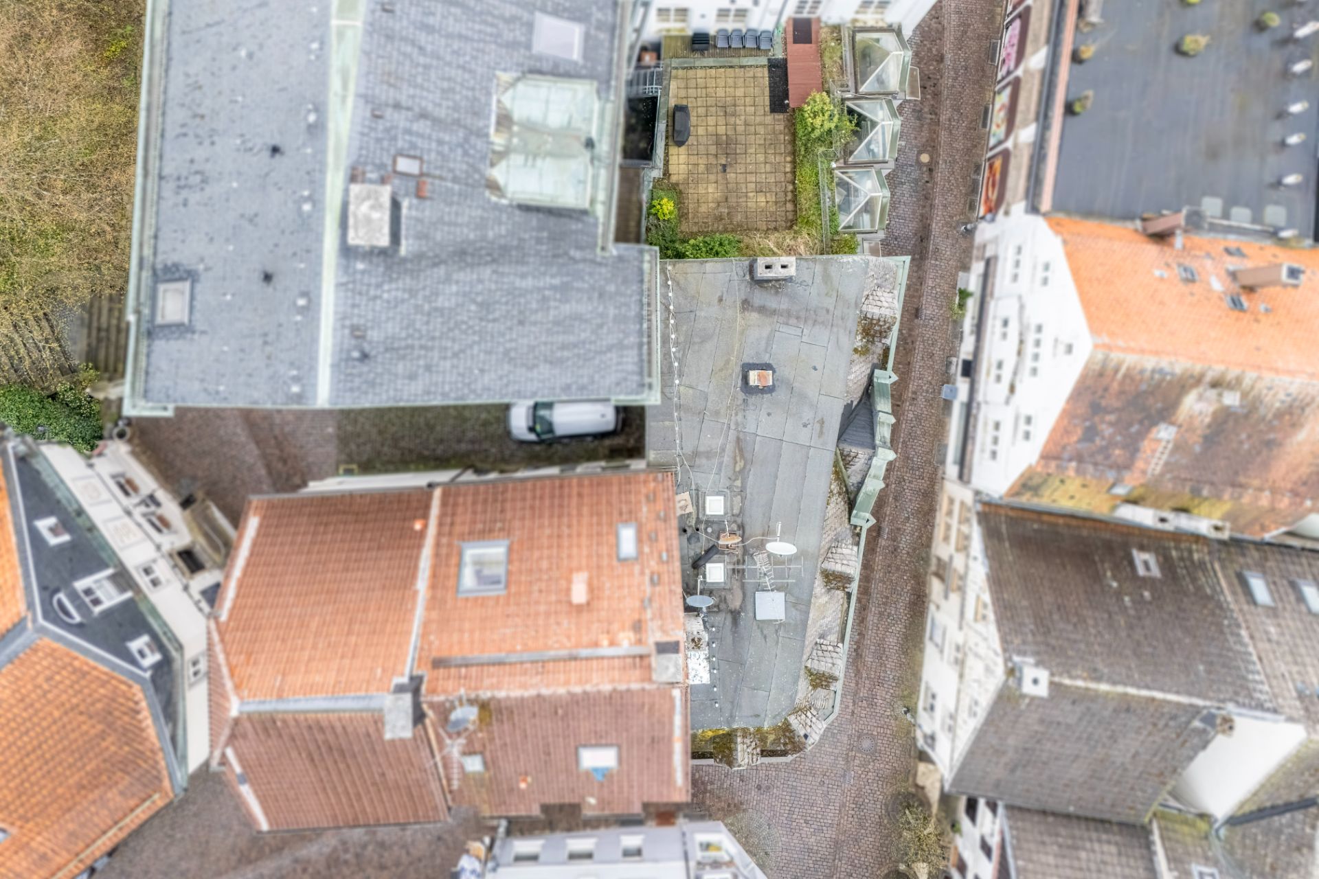 Draufsicht auf mehrere Wohnhäuser mit Innenhöfen und schmaler, gepflasterter Straße dazwischen.