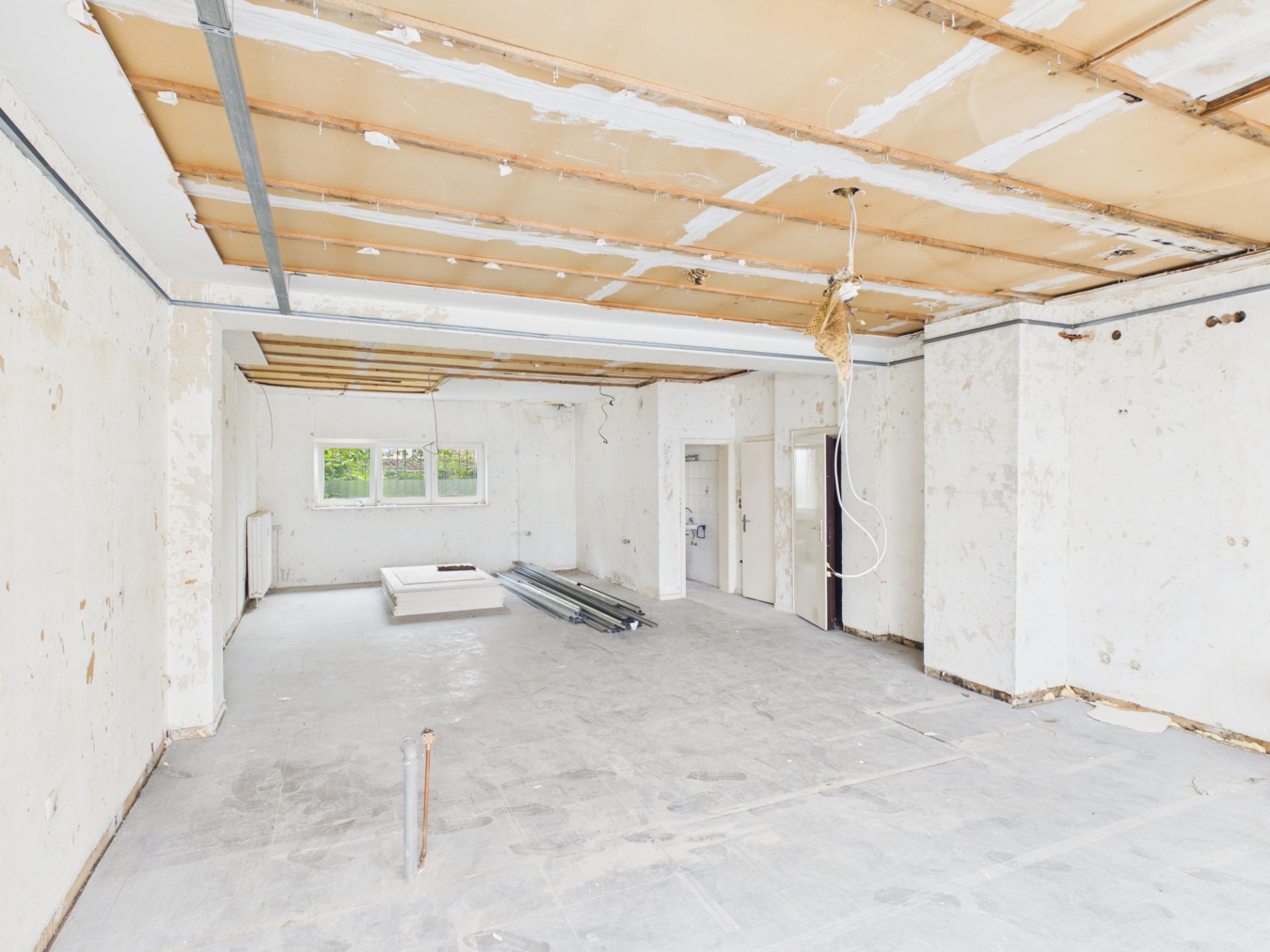 Großer, leerer Raum im Rohbau mit sichtbarer Decke und Baumaterialien auf dem Boden.