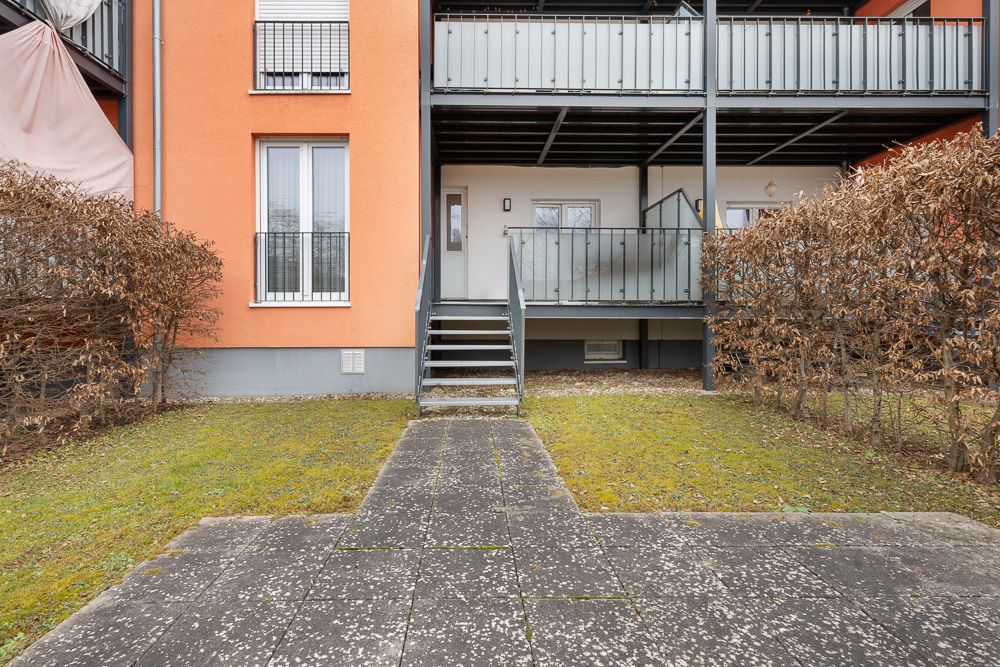Außenansicht eines Wohngebäudes mit Treppe, Balkon und kleinem Garten.