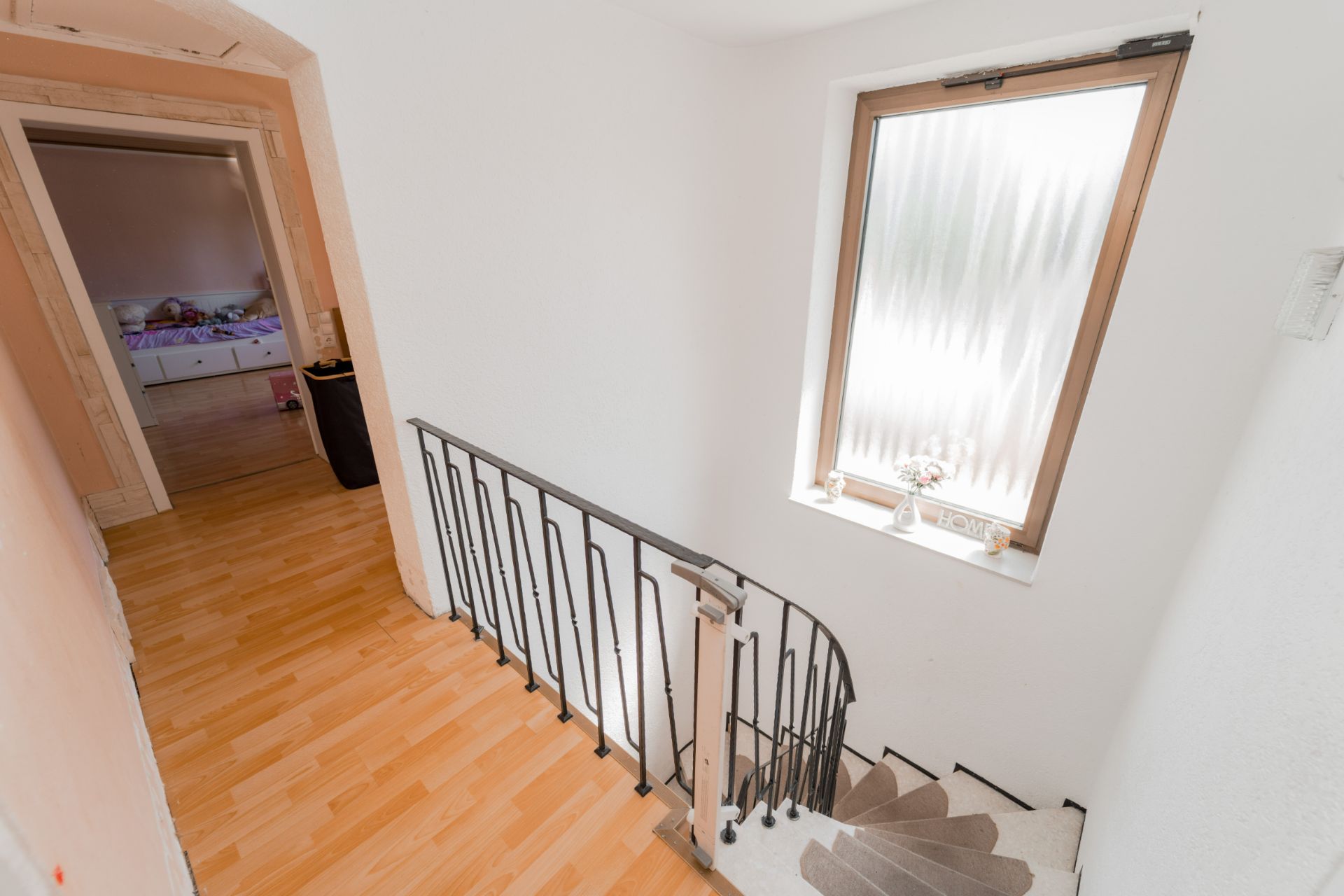 Heller Flur mit Treppe, Fenster und Blick in ein Zimmer mit Bett.