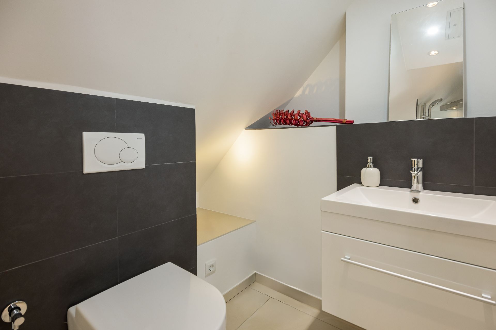 Modernes Badezimmer mit Toilette, Waschbecken und Spiegel unter einer Dachschräge.