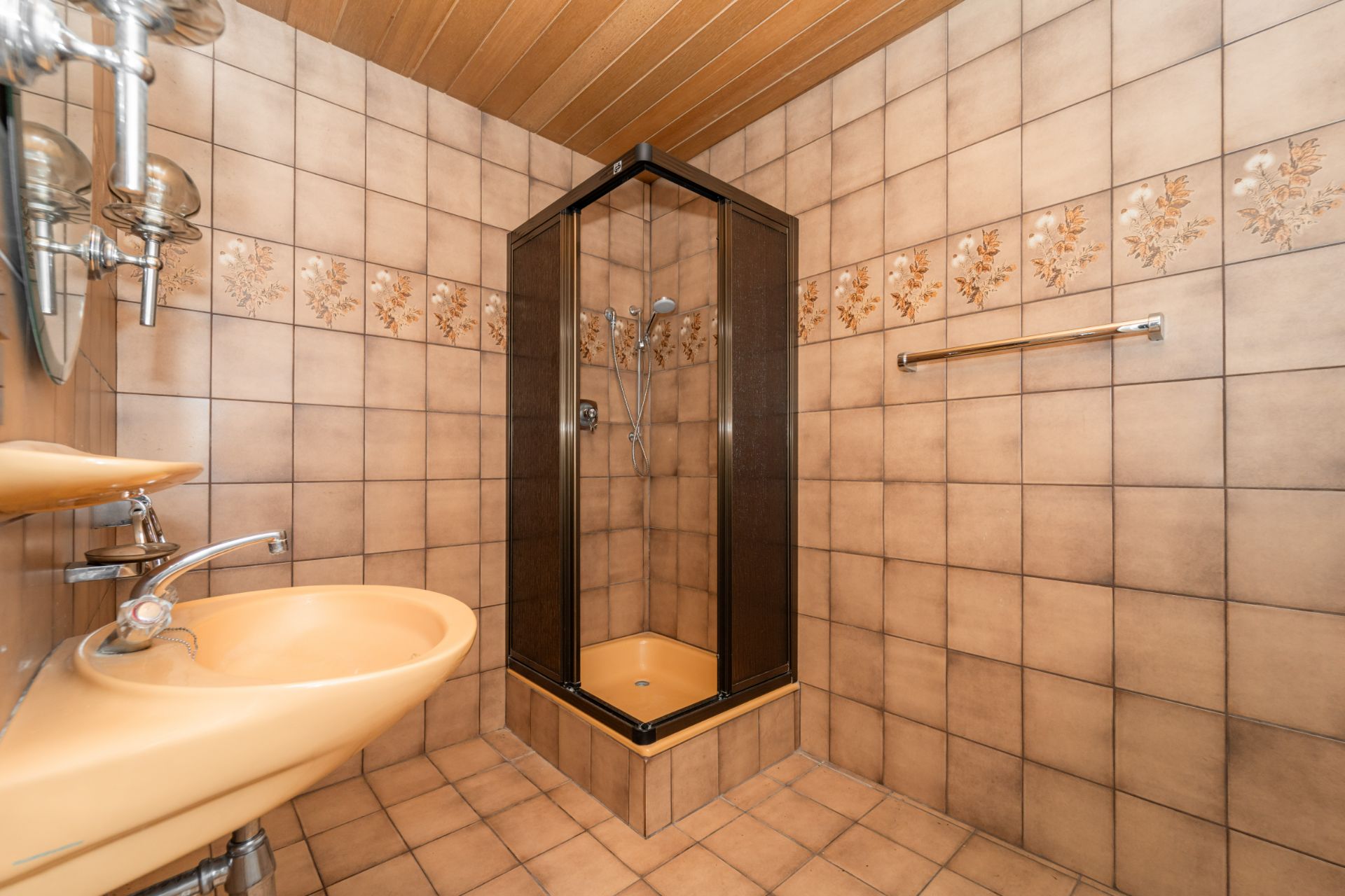 Badezimmer mit beiger Fliesengestaltung, Waschbecken und eckiger Duschkabine.