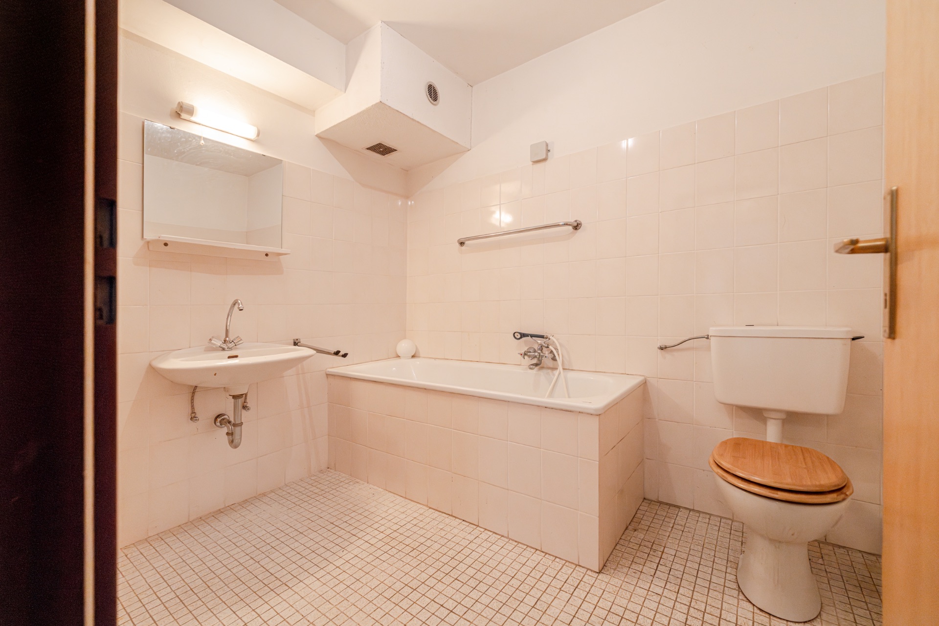 Helles Badezimmer mit Badewanne, Waschbecken, Spiegel und Toilette mit Holzsitz.