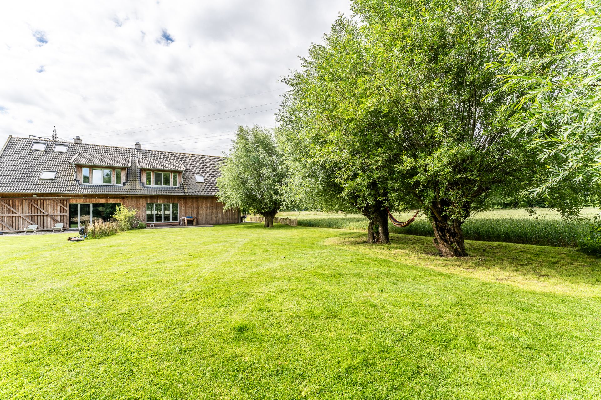 Großer Garten mit Rasen, Bäumen und einer Hängematte, im Hintergrund ein Wohnhaus aus Holz.