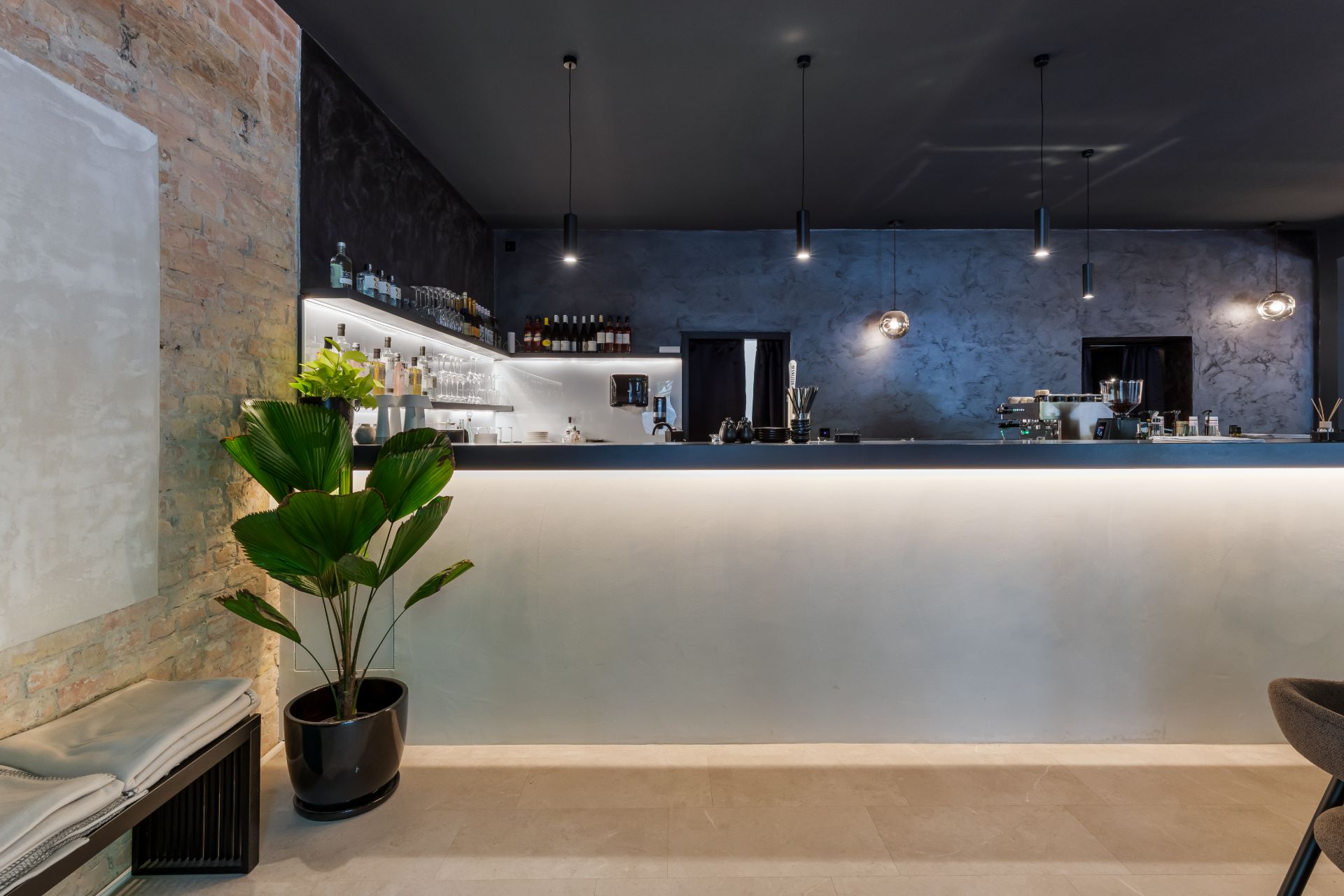 Moderne Hausbar mit beleuchtetem Tresen, Hockern, Regal mit Flaschen und einer großen Pflanze in der Ecke.