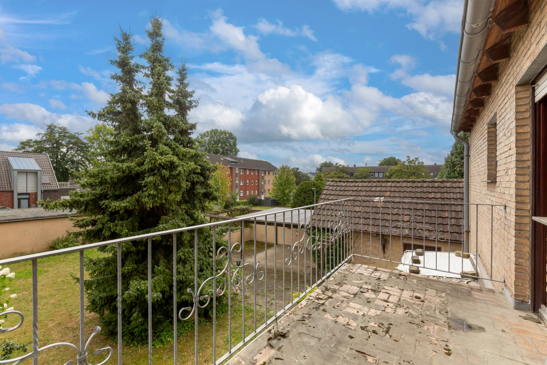 Balkon mit Metallgeländer, Blick auf Garten, Bäume und Nachbarhäuser bei Tageslicht.