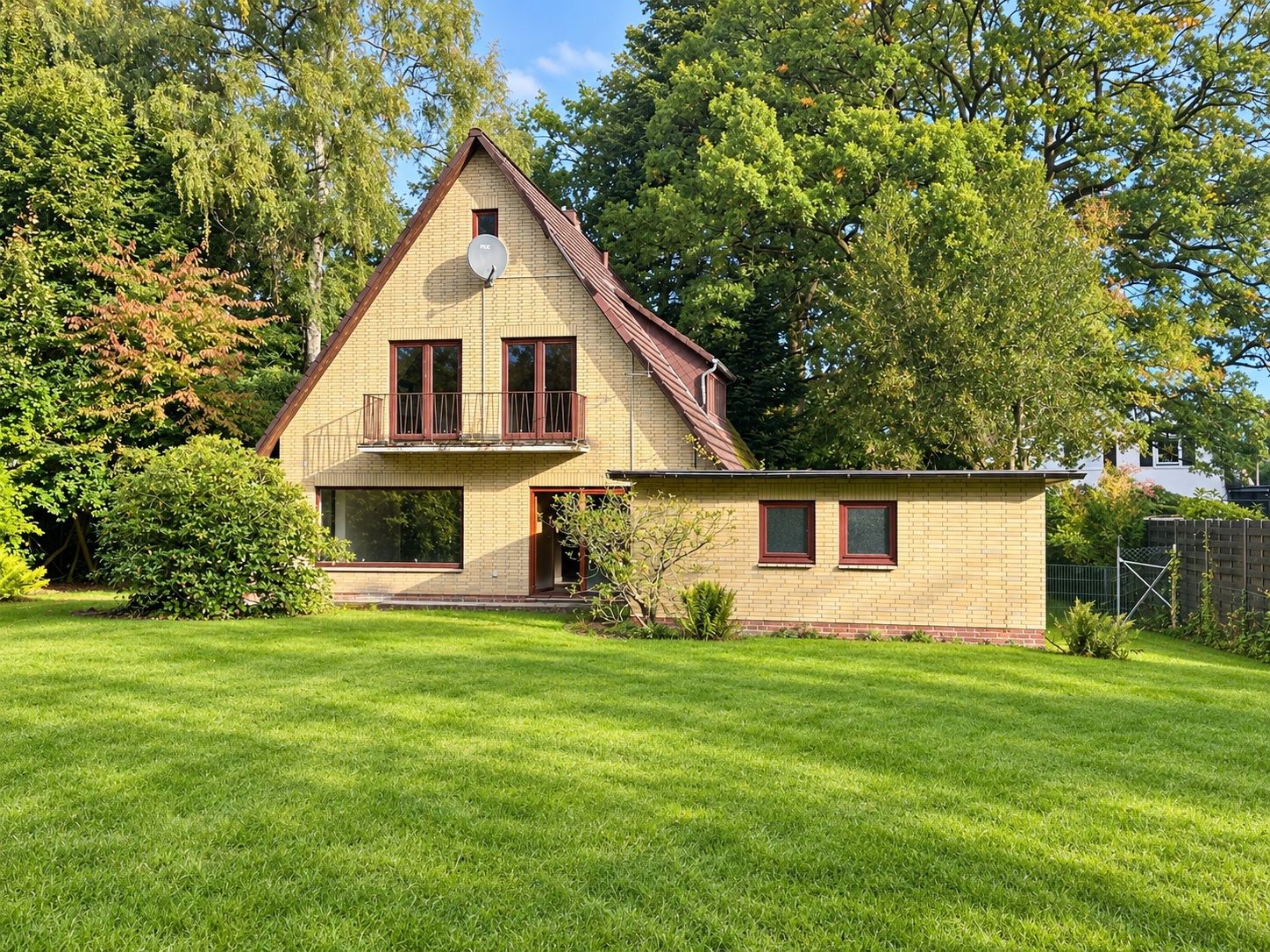 Zweistöckiges Haus mit spitzem Dach und großem Garten, umgeben von Bäumen.