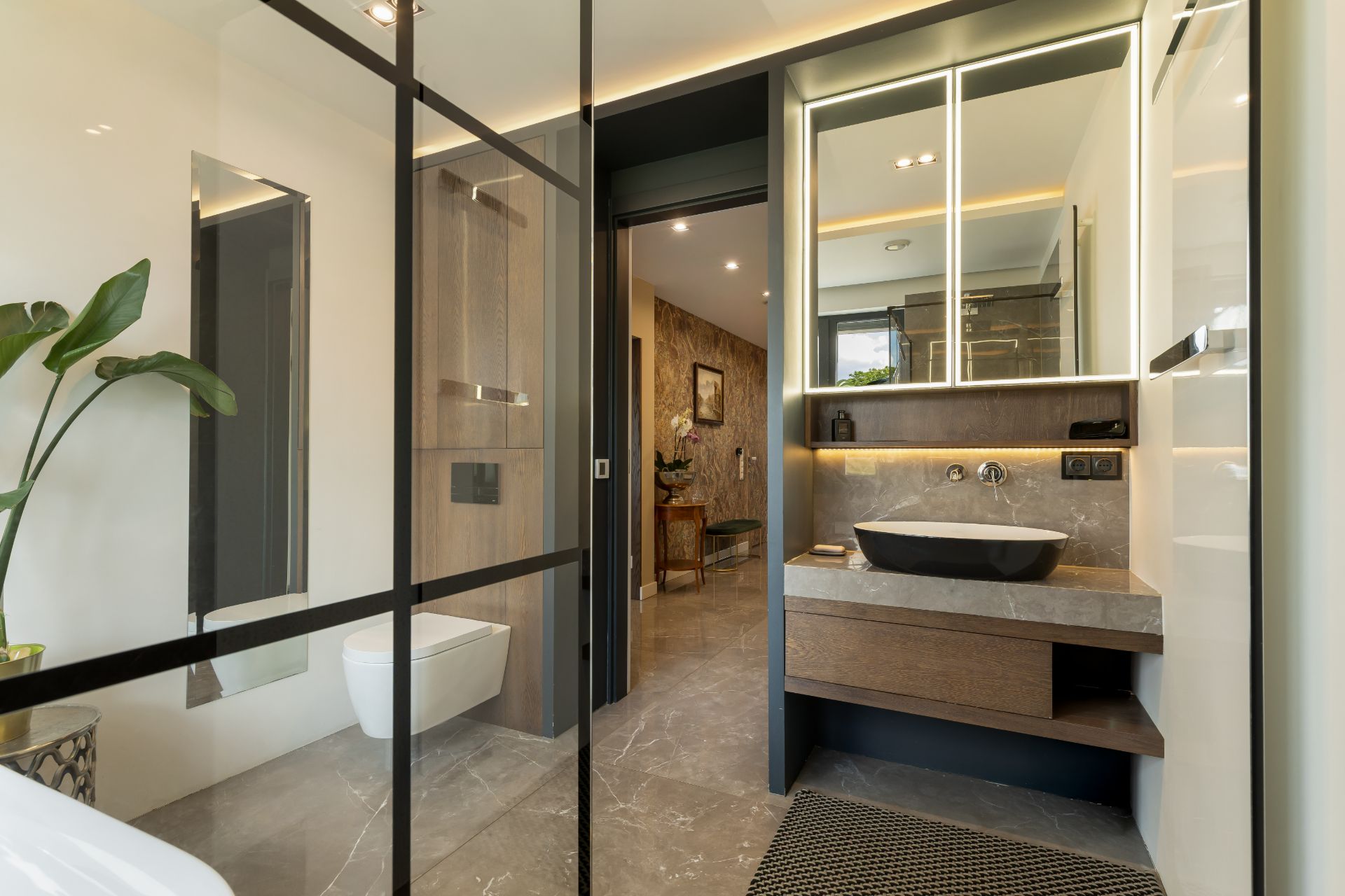 Modernes Badezimmer mit Spiegel, Waschbecken, WC und Pflanze, Blick in den Flur.