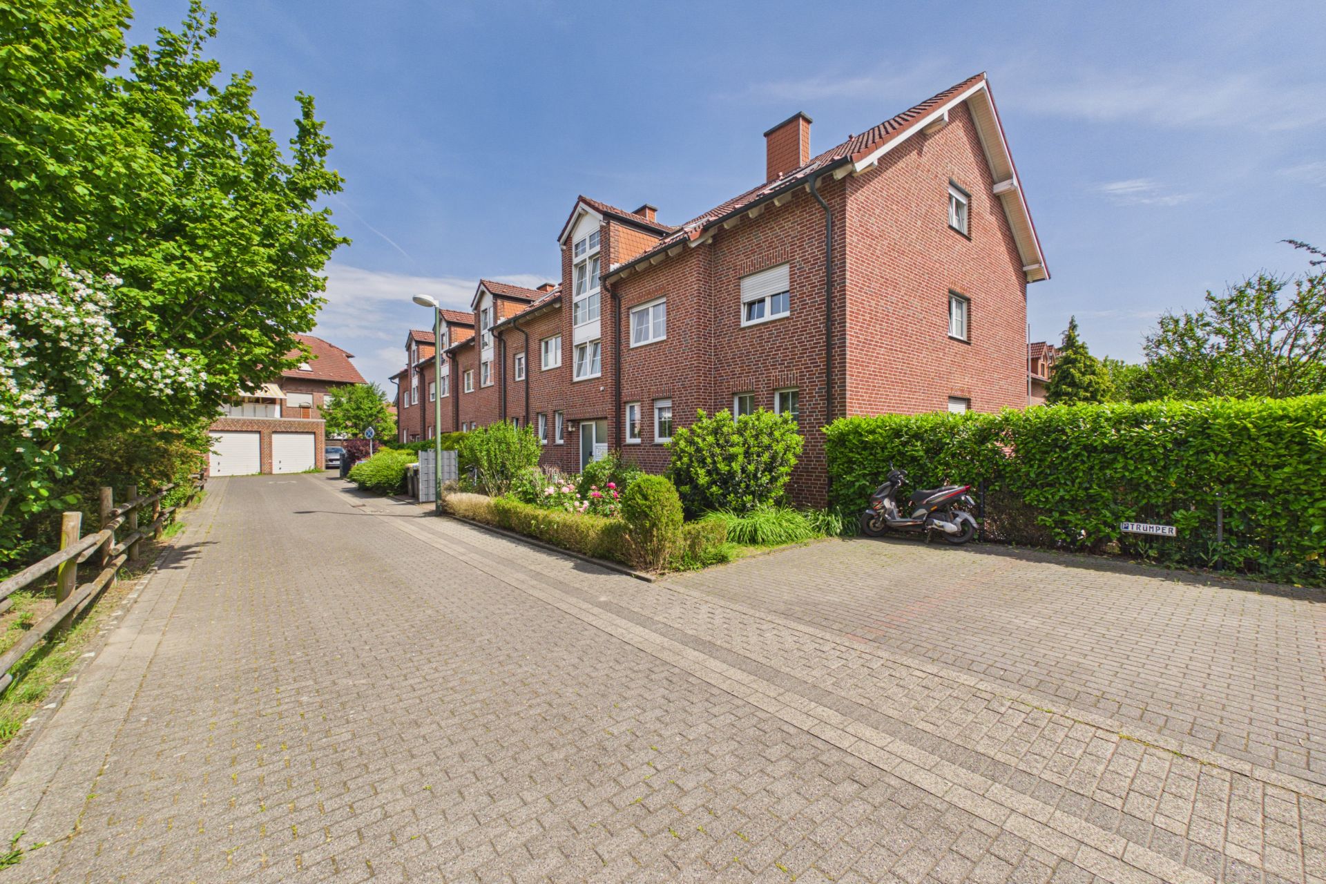 Zweistöckiges rotes Wohngebäude mit Garten und Straße im Vordergrund, Motorrad am Rand geparkt.