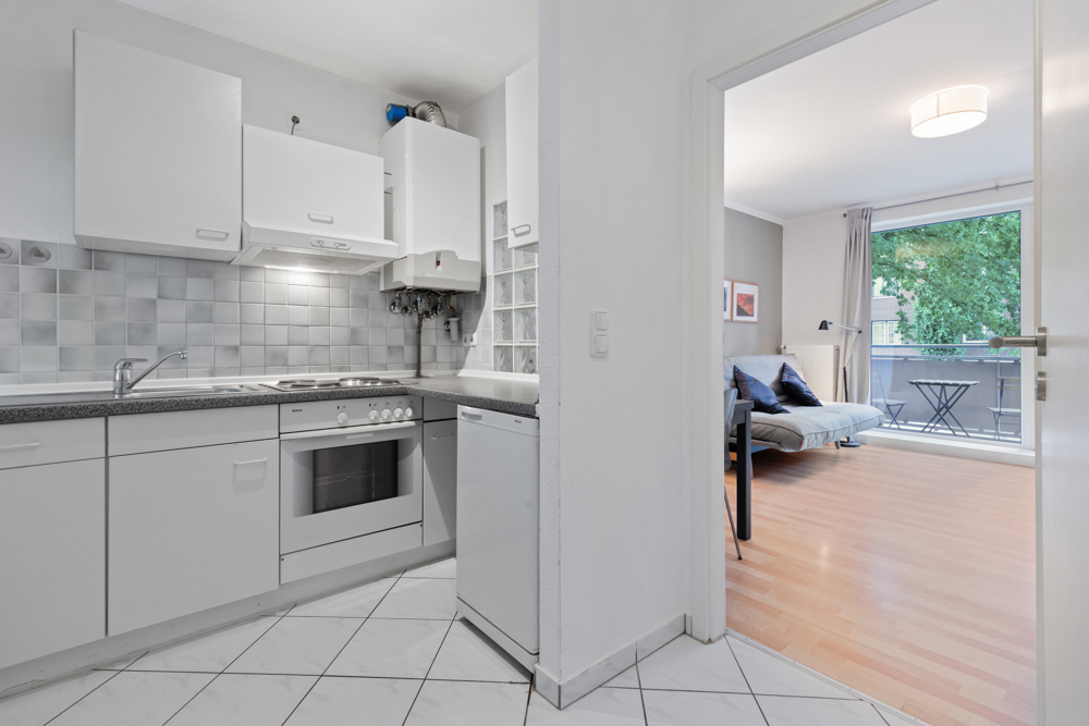 Helle Küche mit weißen Schränken und Blick ins Wohnzimmer mit Sofa und Balkon.