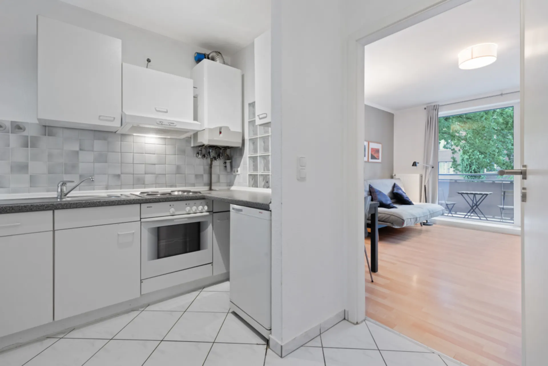 Helle Küche mit weißen Schränken und Blick ins Wohnzimmer mit Sofa und Balkon.