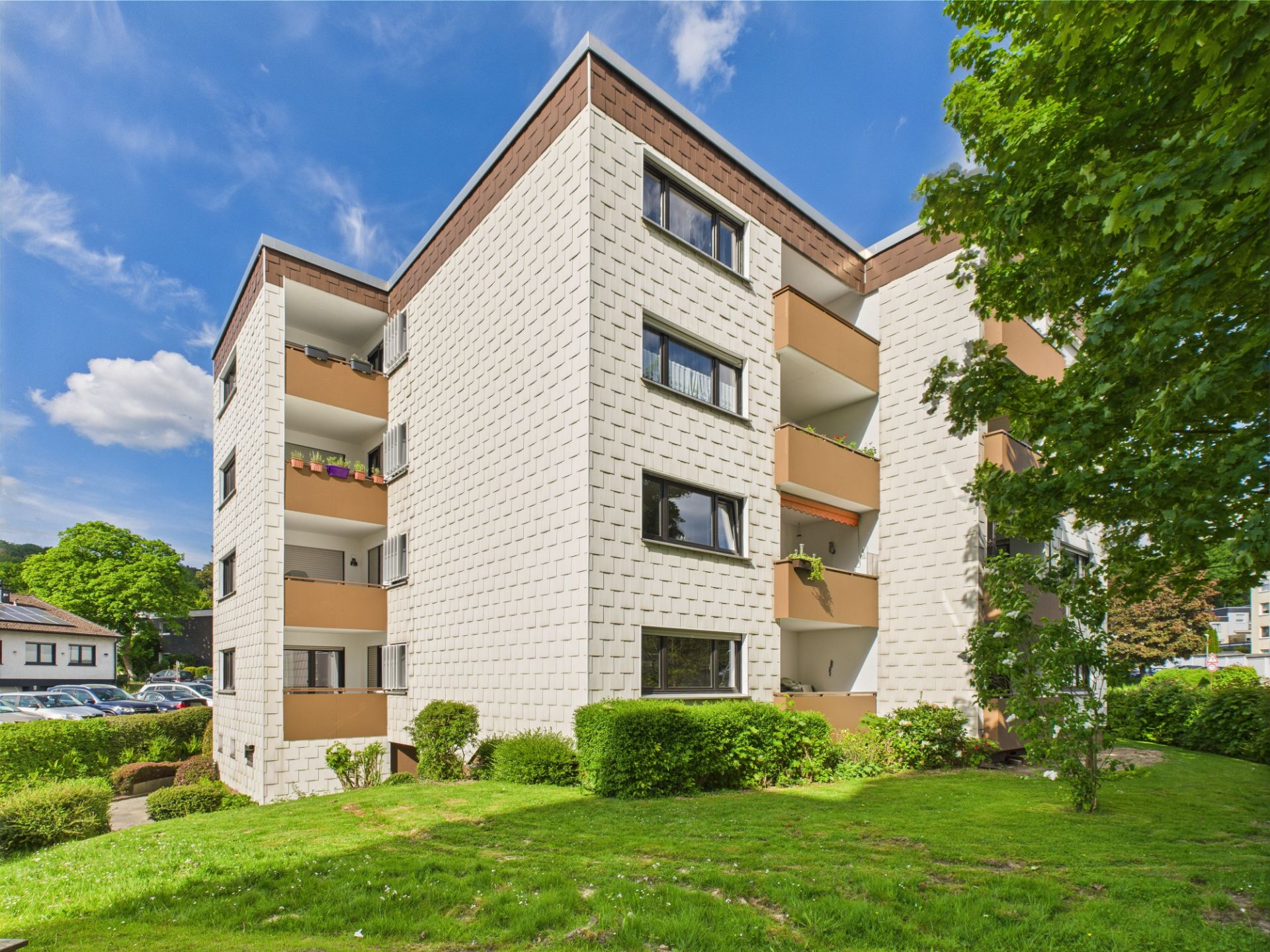 Vierstöckiges Wohnhaus mit Balkonen, umgeben von Grünfläche und Bäumen.