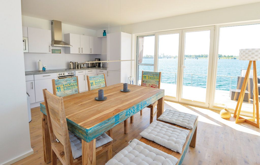 Helle Wohnküche mit Holztisch, Stühlen, Küchengeräten und großem Fenster mit Wasserblick.