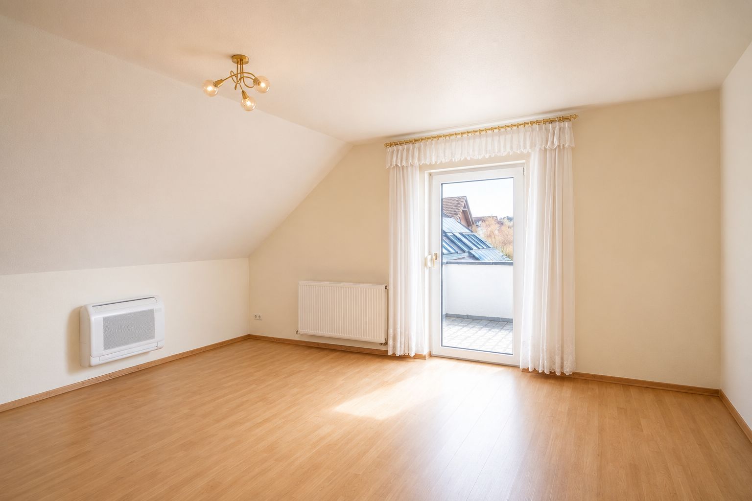 Heller, leerer Raum mit Holzboden, Tür zum Balkon und Heizkörper an der Wand.