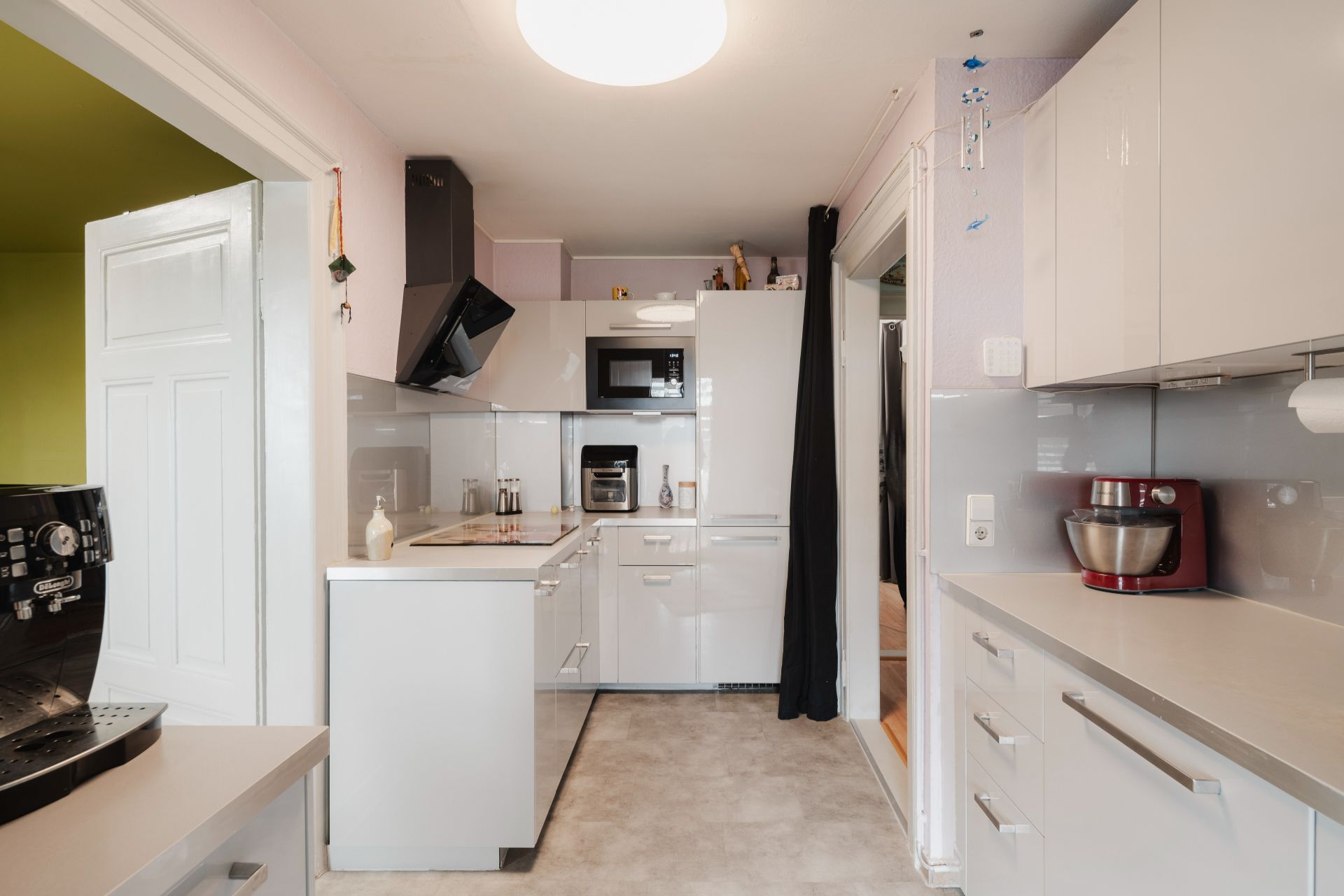 Moderne Küche mit weißen Hochglanzschränken, Kaffeemaschine, Küchenmaschine und Mikrowelle.