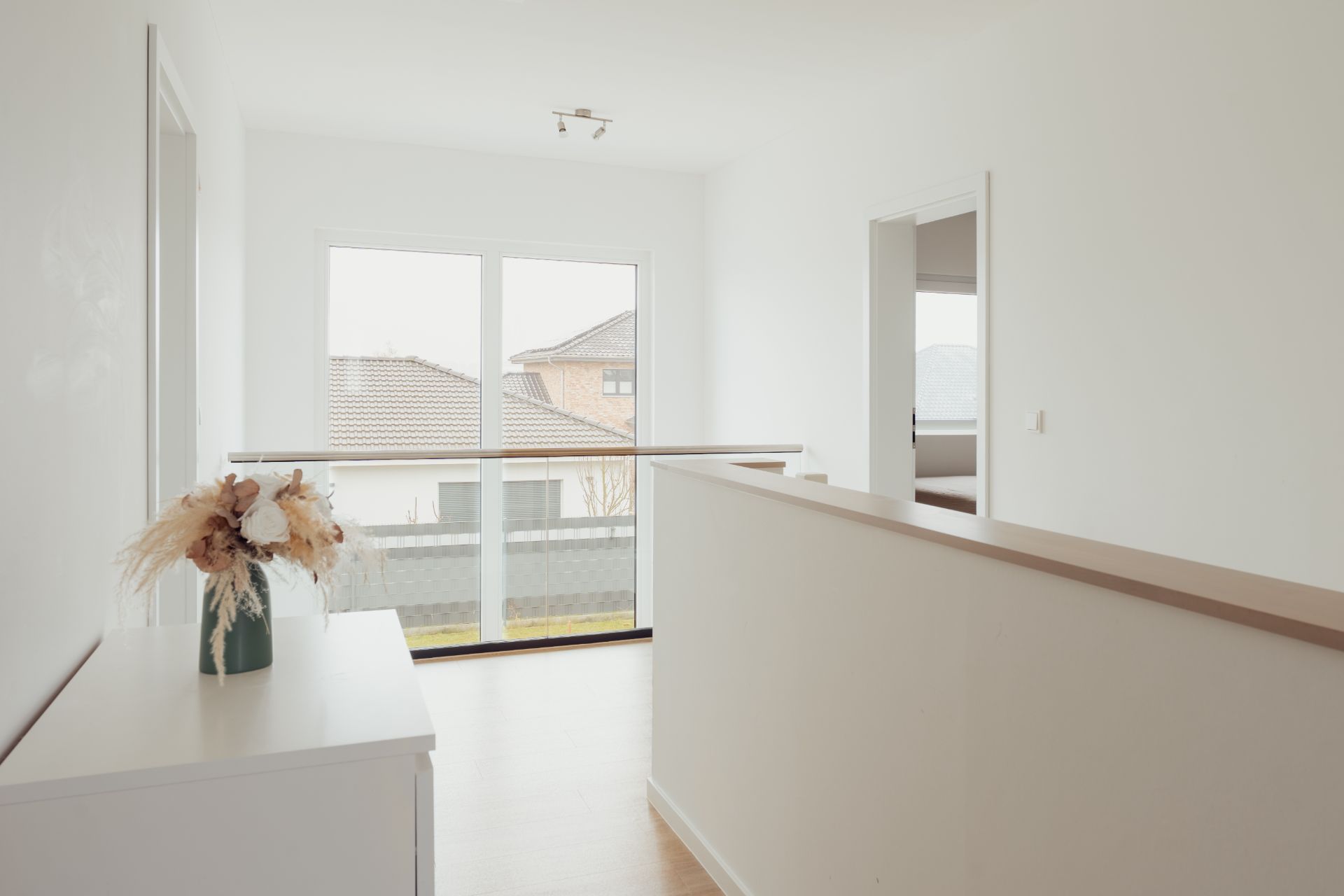 Heller Flur mit Fenster, Kommode mit Vase und Zugang zu einem weiteren Zimmer.