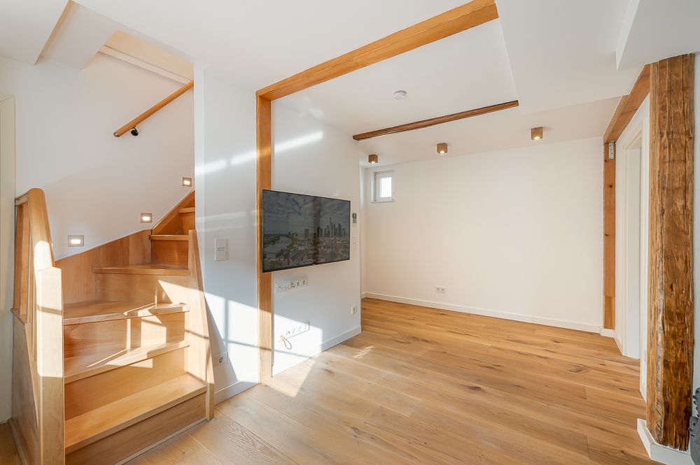 Helles Wohnzimmer mit Holztreppe, TV an der Wand und Holzboden.